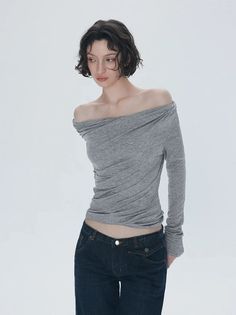 Woman with short curly hair wearing an off-shoulder top and dark wash jeans