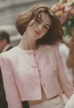 Woman with short brown hair wearing a pink cropped jacket and shoulder bag