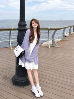 Woman in a white dress and purple cardigan standing on a pier by the ocean