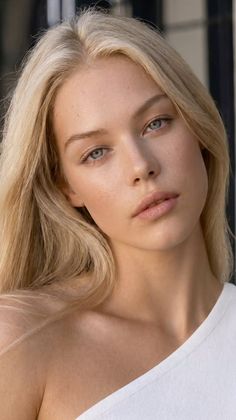 Blonde woman with blue eyes in a white top, looking directly at the camera