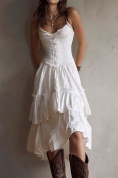 Woman in a white corset dress and cowboy boots leaning against a wall