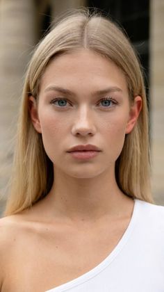 Blonde woman with blue eyes wearing a white top, looking directly at the camera