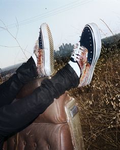 Legs in black jeans and studded shoes resting on a brown leather seat outdoors