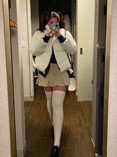Woman in a white puffer jacket and pleated skirt taking a mirror selfie