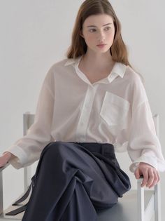 Woman with long hair wearing a white shirt and dark pants, sitting indoors