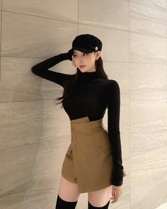 Woman in a black turtleneck and brown skirt with a newsboy cap indoors