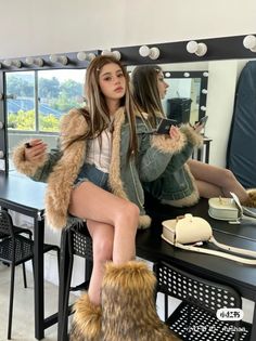 Woman in a fur-trimmed denim jacket and short shorts sitting on a table