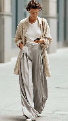 Woman in wide leg pants and a long shirt walking outdoors while looking at her phone