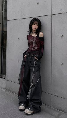 Person with black shaggy hair wearing a gothic-style outfit against a concrete wall