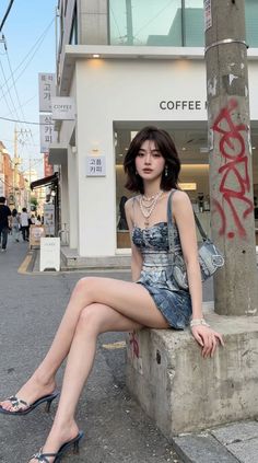Woman in a denim dress and heels sitting on a concrete block on a street