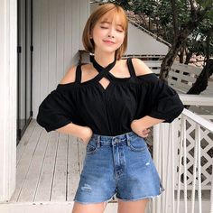 Woman with short blonde hair wearing an off-shoulder top and denim shorts outdoors