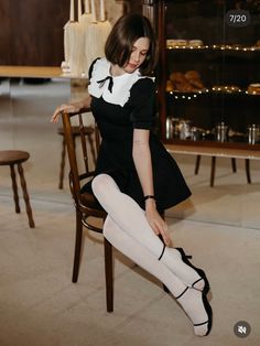 Woman in a black dress with a white collar and white tights sitting indoors