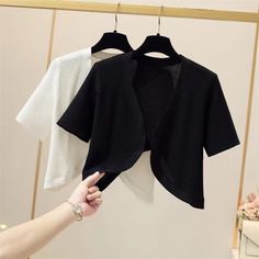 Black and white short sleeve knitted shrugs on hangers, with a hand reaching out