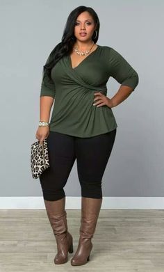 Woman with long dark hair wearing a green top, black pants, and brown boots
