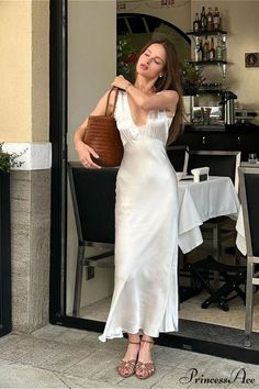 Woman in a white dress holding a brown bag outside a cafe