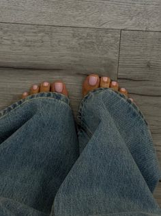 Bare feet with pink nail polish peeking out from light wash jeans on a wooden floor