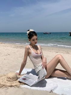 Woman in a white tank top and bikini top sitting on a beach