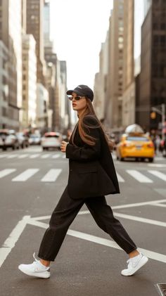 Woman in a black blazer and baseball cap crossing a city street