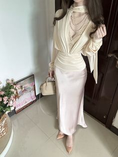 Woman in a beige lace top and satin skirt with pearl necklaces and a handbag