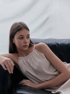 Young woman with long hair wearing a sleeveless top, sitting on a dark couch