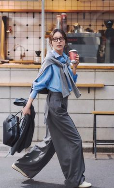 Woman in a blue shirt and wide leg pants walking with a coffee cup