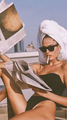 Woman with a towel on her head and sunglasses reading a newspaper outdoors