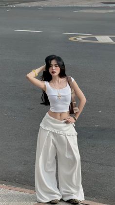 Woman with long black hair in a white crop top and wide leg pants on a street