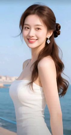 Woman in a white dress with long hair and earrings smiling outdoors by the ocean