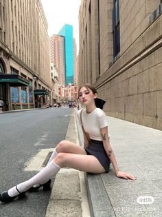 Woman in a short skirt and white socks sitting on a city sidewalk