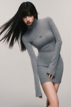 Woman with long dark hair wearing a gray turtleneck dress with a butterfly pin