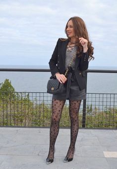 Woman in a black blazer and star pattern tights standing outdoors by the sea