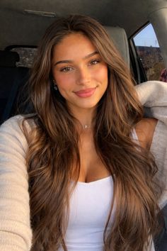 Woman with long brown hair wearing a white top and choker, smiling at the camera
