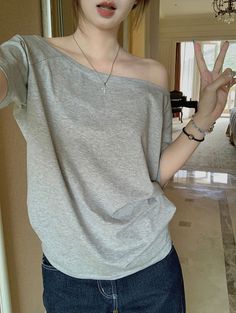 Person in an off-shoulder gray top and jeans making a peace sign