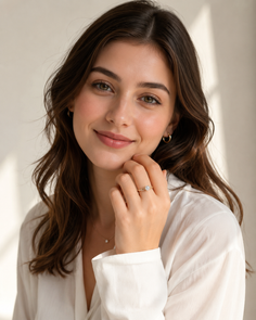 Woman with long brown hair wearing a white shirt and jewelry, smiling indoors