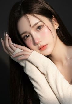 Woman with long dark hair and a white sweater posing against a dark background