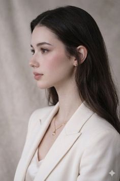 Woman with long dark hair wearing a white blazer and gold necklace