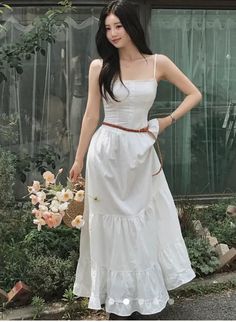 Woman in a white dress holding a straw bag with pink flowers outdoors