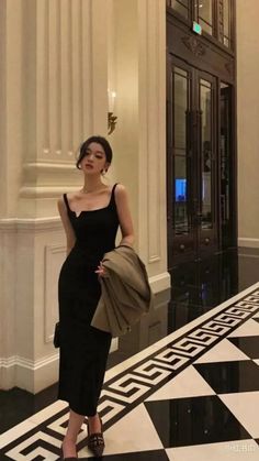 Woman in a black dress and high heels standing in an elegant indoor setting