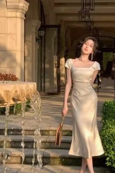 Woman in a satin dress standing next to a fountain in soft golden hour light