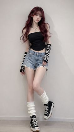 Woman with long wavy red hair wearing a black tube top and denim shorts