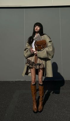 Woman in a trench coat and pleated skirt holding a newspaper and bag outdoors