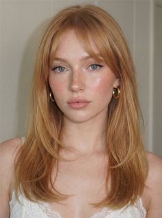 Woman with red hair and freckles wearing a white lace top and hoop earrings