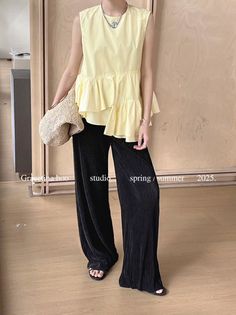 Person in a yellow ruffle top and black wide-leg pants holding a straw bag