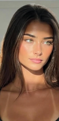Woman with long brown hair and green eyes, wearing a gold necklace