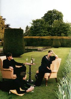 Three people in dark clothing relaxing in a formal garden with wine
