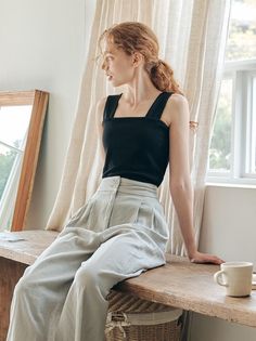 Woman with red hair in a black top and wide leg pants sitting indoors