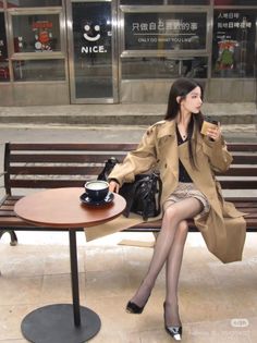 Woman in a trench coat and plaid skirt sitting at an outdoor cafe