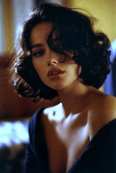 Woman with short curly dark hair and exposed shoulders in soft lighting