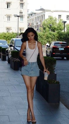 Woman in a white tank top and denim skirt walking on a street