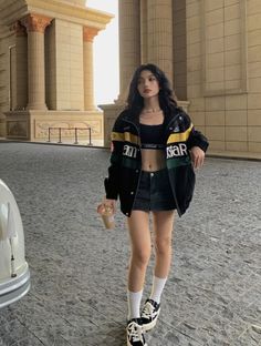 Woman in a crop top and denim skirt with a bomber jacket outdoors
